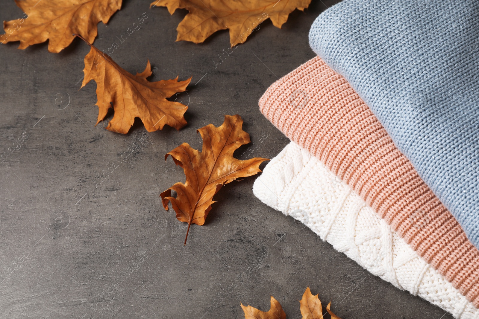 Photo of Stack of folded knitted sweaters and autumn leaves on table. Space for text