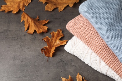 Photo of Stack of folded knitted sweaters and autumn leaves on table. Space for text