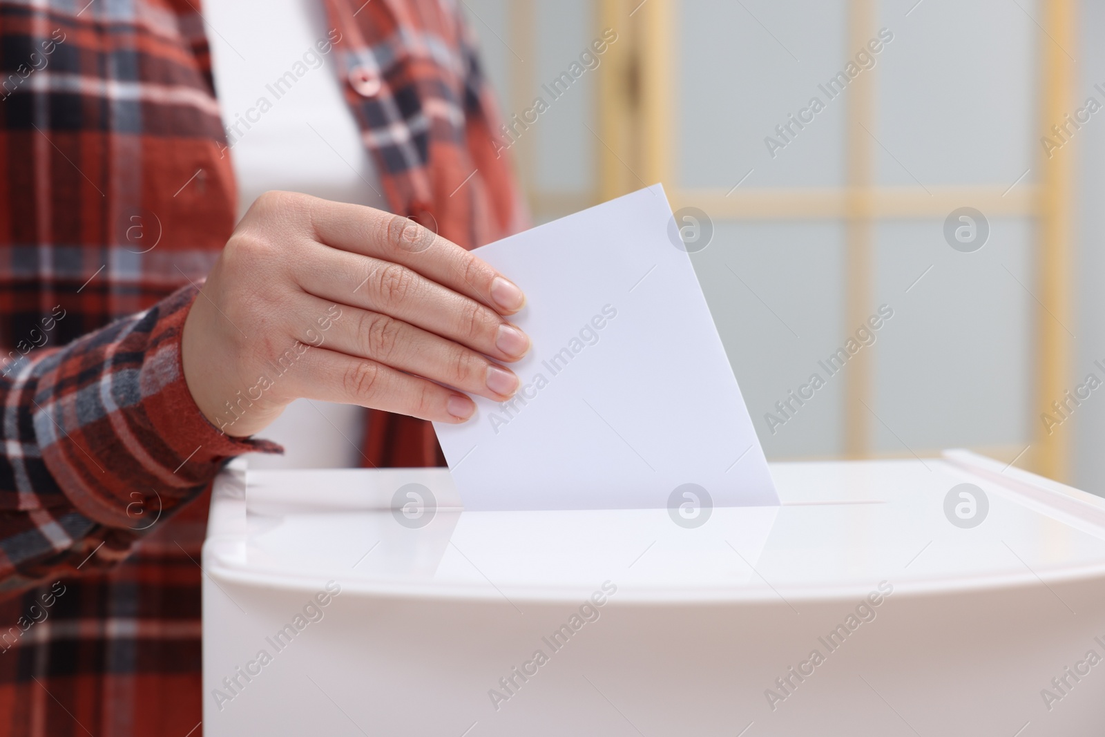 Photo of Woman putting her vote into ballot box on blurred background, closeup