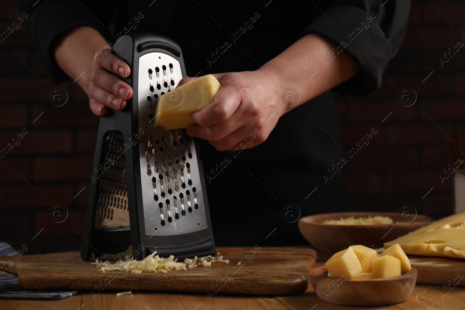 Photo of Woman grating cheese at wooden table, closeup