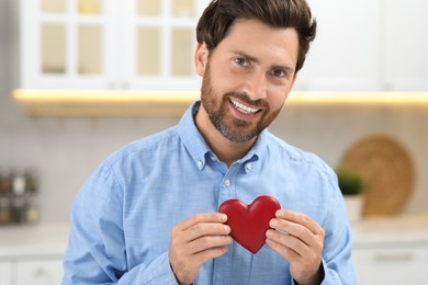 Happy bearded man holding red heart indoors