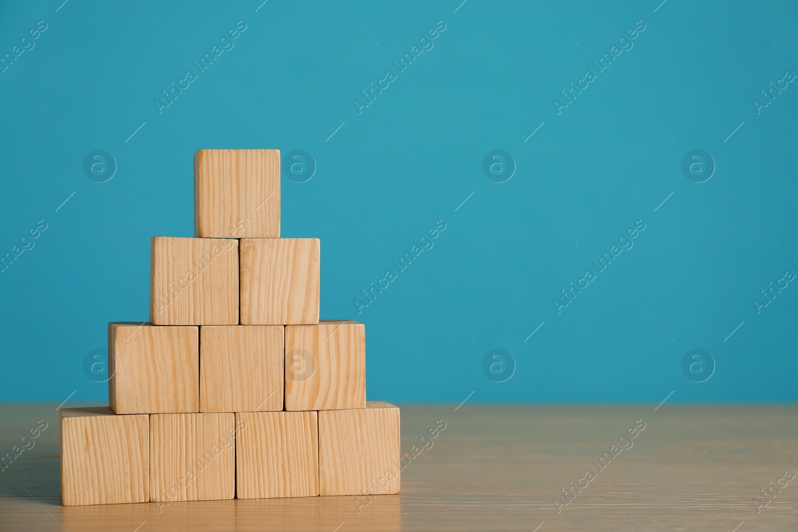 Photo of Pyramid of blank cubes on wooden table against light blue background. Space for text