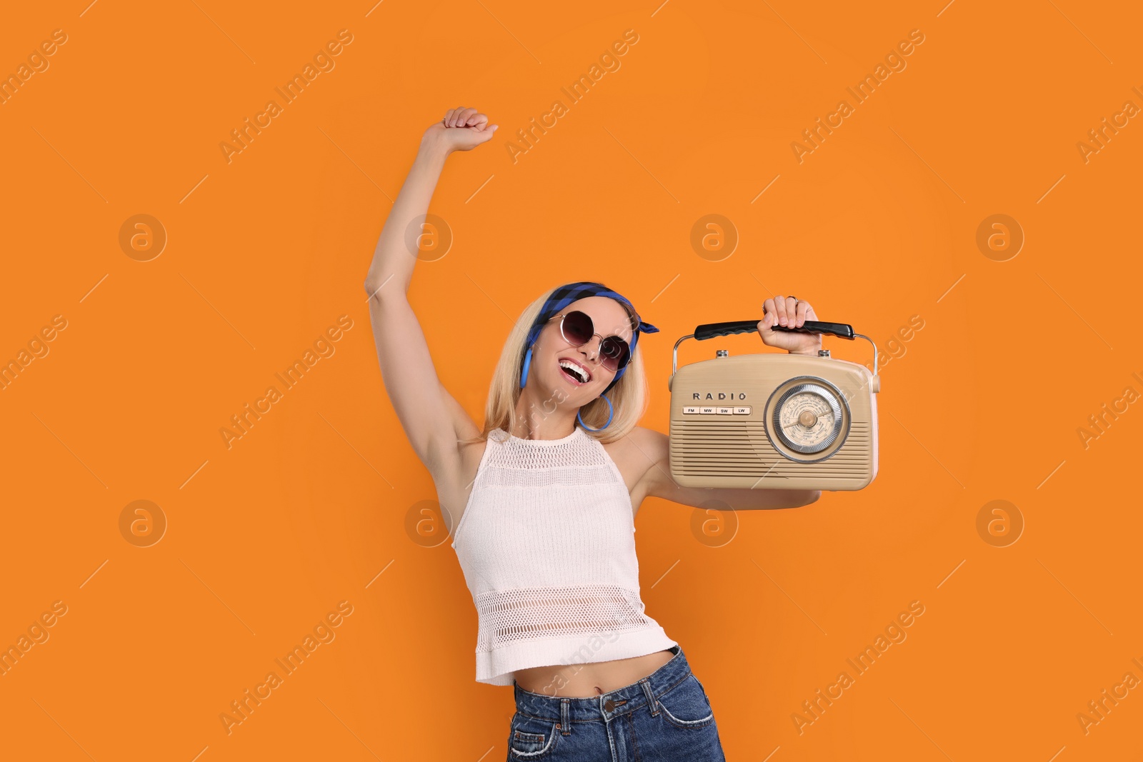 Photo of Happy hippie woman with retro radio receiver dancing on orange background