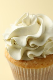 Photo of Tasty vanilla cupcake with cream on pale yellow background, closeup