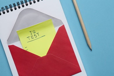 Photo of Note with text IQ Test in envelope, notepad and pencil on light blue background, flat lay
