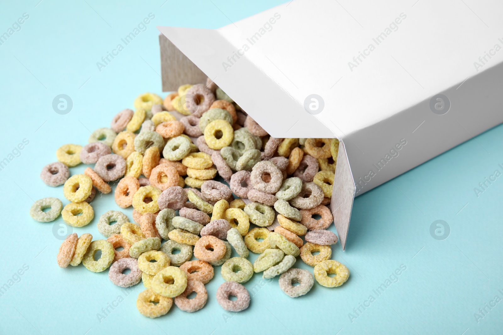 Photo of Paper box with tasty cereal rings on light blue background, closeup