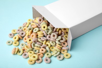 Photo of Paper box with tasty cereal rings on light blue background, closeup