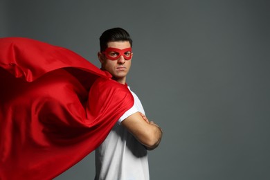 Man wearing superhero cape and mask on grey background. Space for text