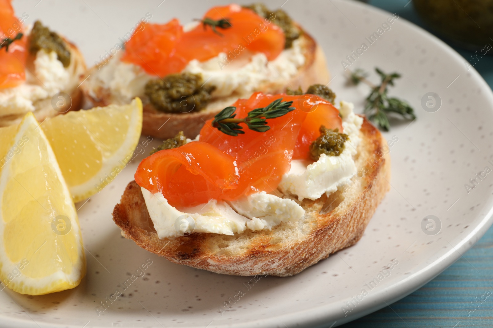 Photo of Delicious bruschettas with cream cheese, salmon and pesto sauce on light blue wooden table, closeup