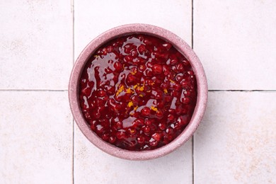 Photo of Tasty cranberry sauce in bowl on white tiled table, top view