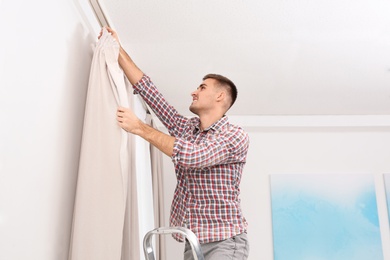 Man hanging window curtain indoors. Interior decor element