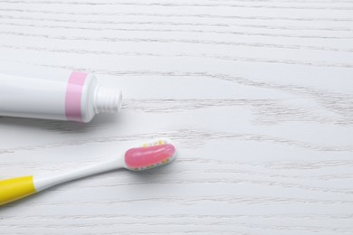 Photo of Brush with toothpaste and tube on white wooden table, flat lay. Space for text