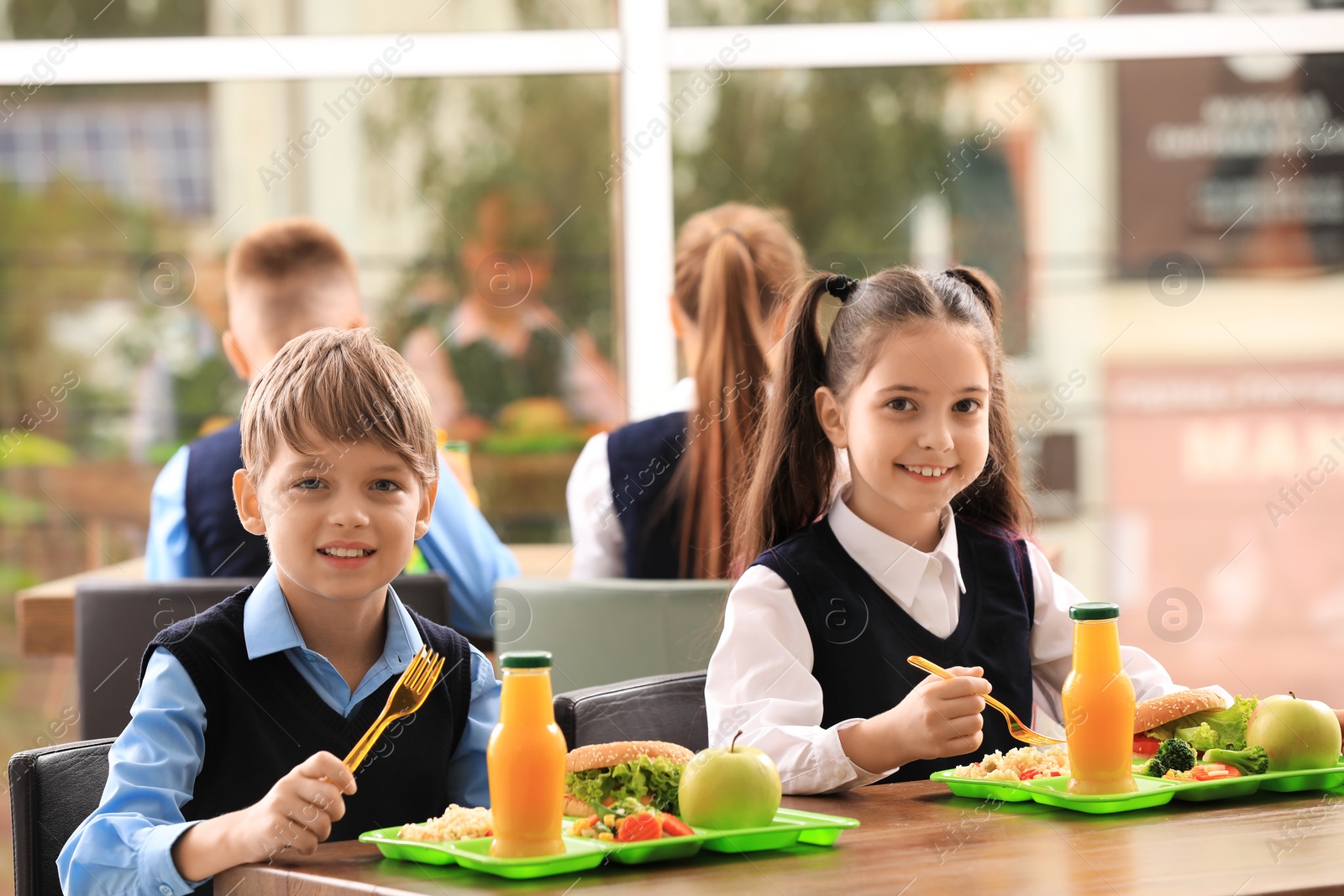 Photo of Happy children at table with healthy food in school canteen