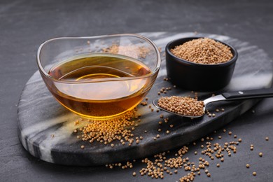 Photo of Bowl of natural oil and mustard seeds on black table