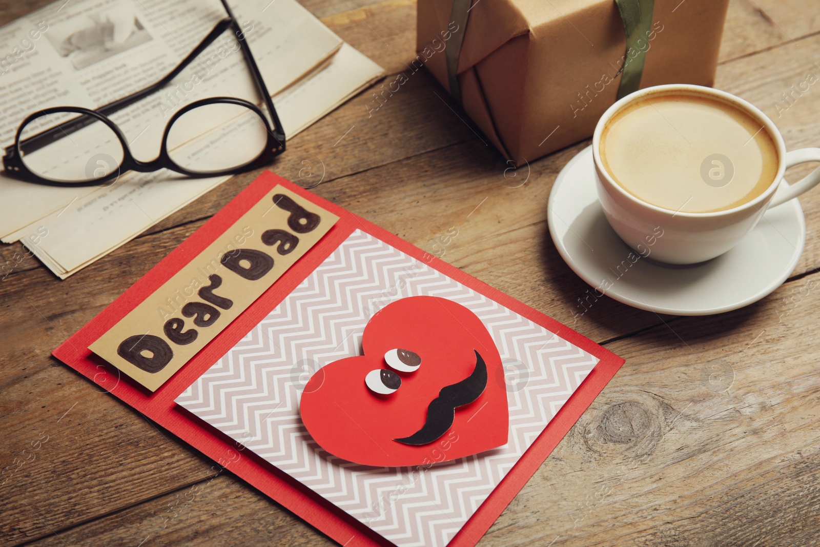 Photo of Handmade card with words DEAR DAD, gift and coffee on wooden table. Happy Father's day