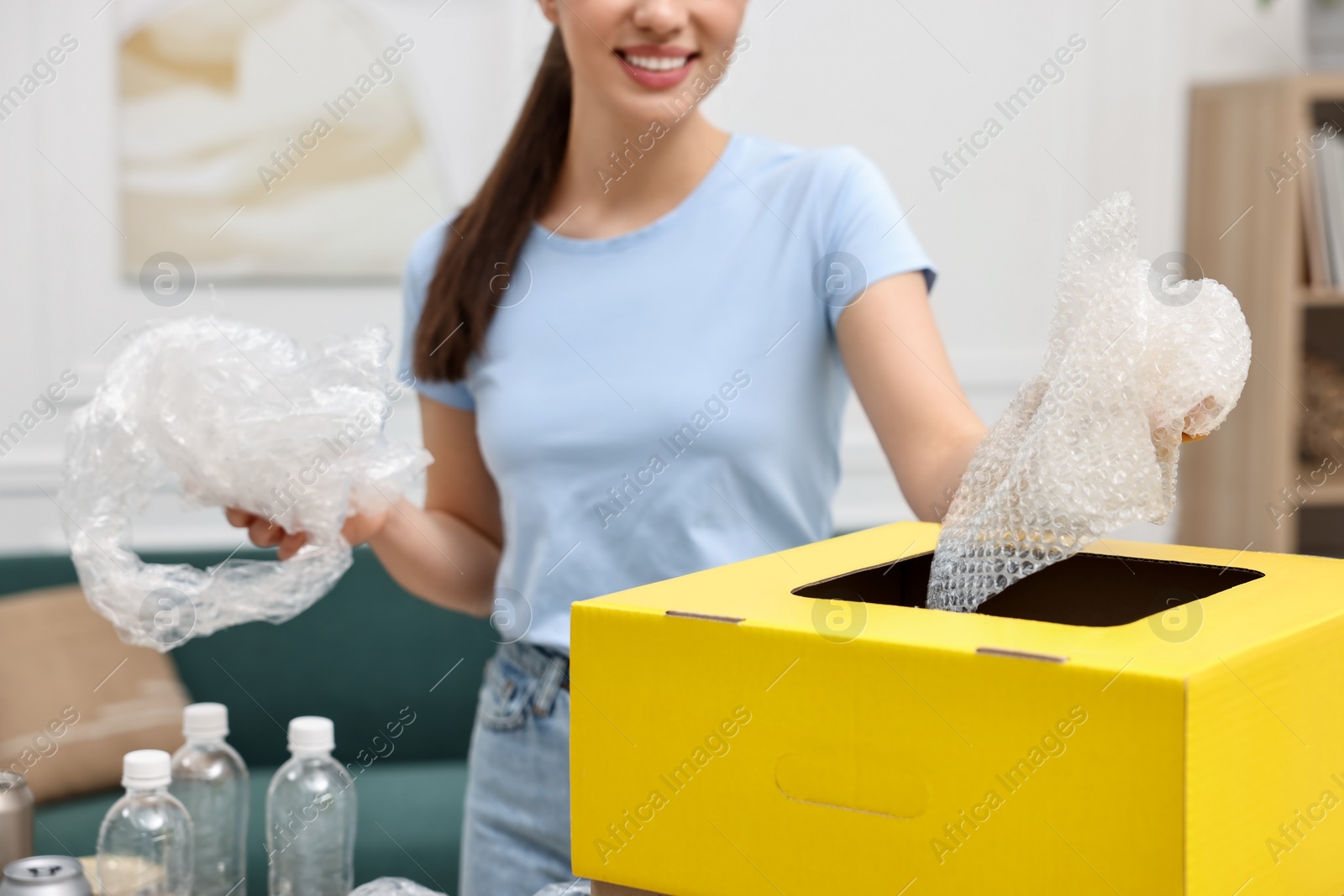 Photo of Garbage sorting. Smiling woman throwing plastic package into cardboard box in room, closeup