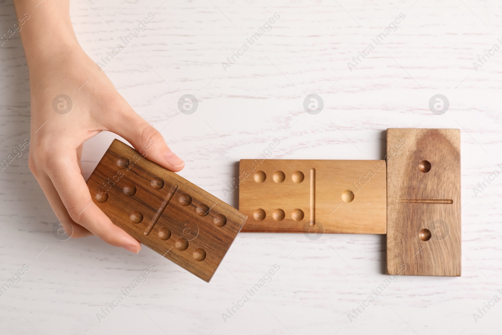 Photo of Woman playing dominoes at white table, top view