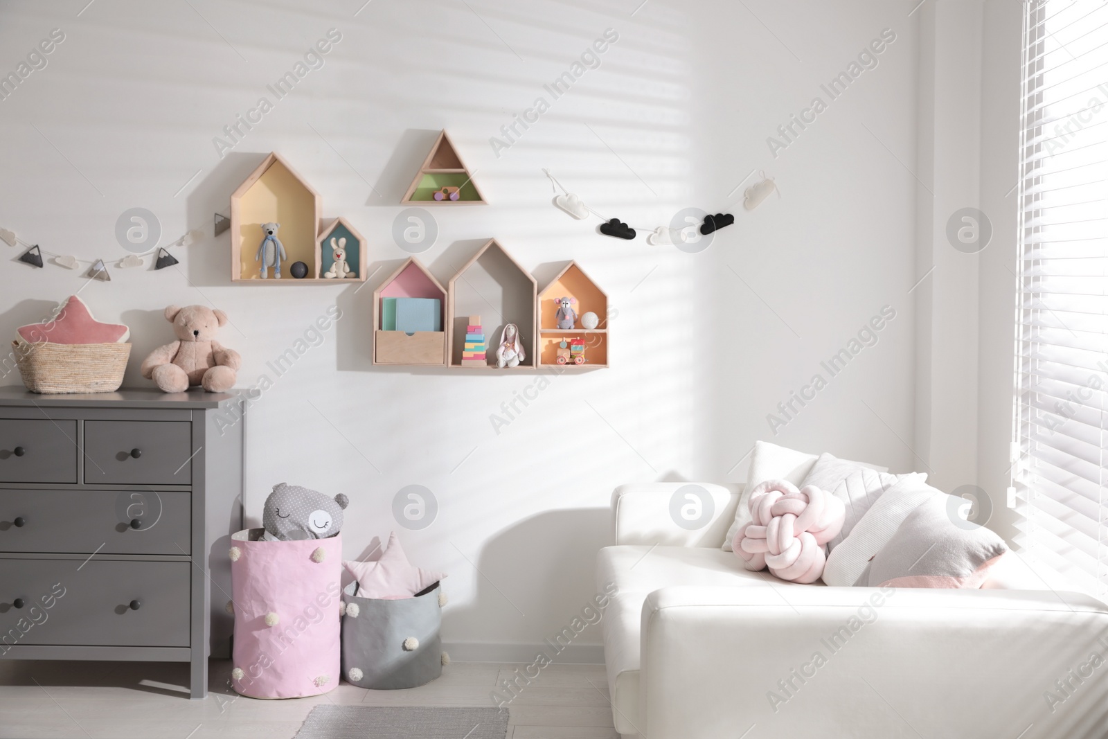 Photo of Cute children's room with house shaped shelves, sofa and chest of drawers. Interior design