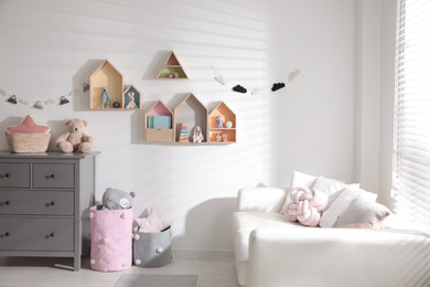 Photo of Cute children's room with house shaped shelves, sofa and chest of drawers. Interior design