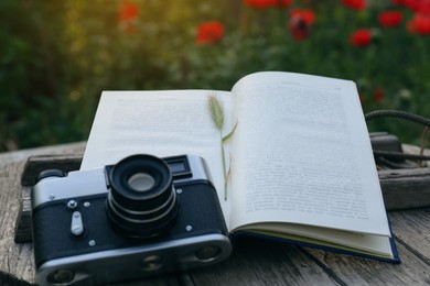 Photo of Open book with spike and vintage camera on wooden table outdoors, closeup