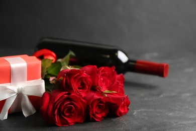 Photo of Beautiful red roses, gift box and bottle of wine on grey table, space for text. Valentine's Day celebration