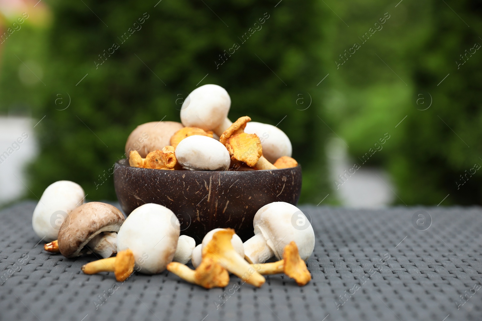 Photo of Bowl with different fresh mushrooms on grey rattan table outdoors. Space for text