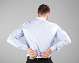 Young man suffering from back pain on light background