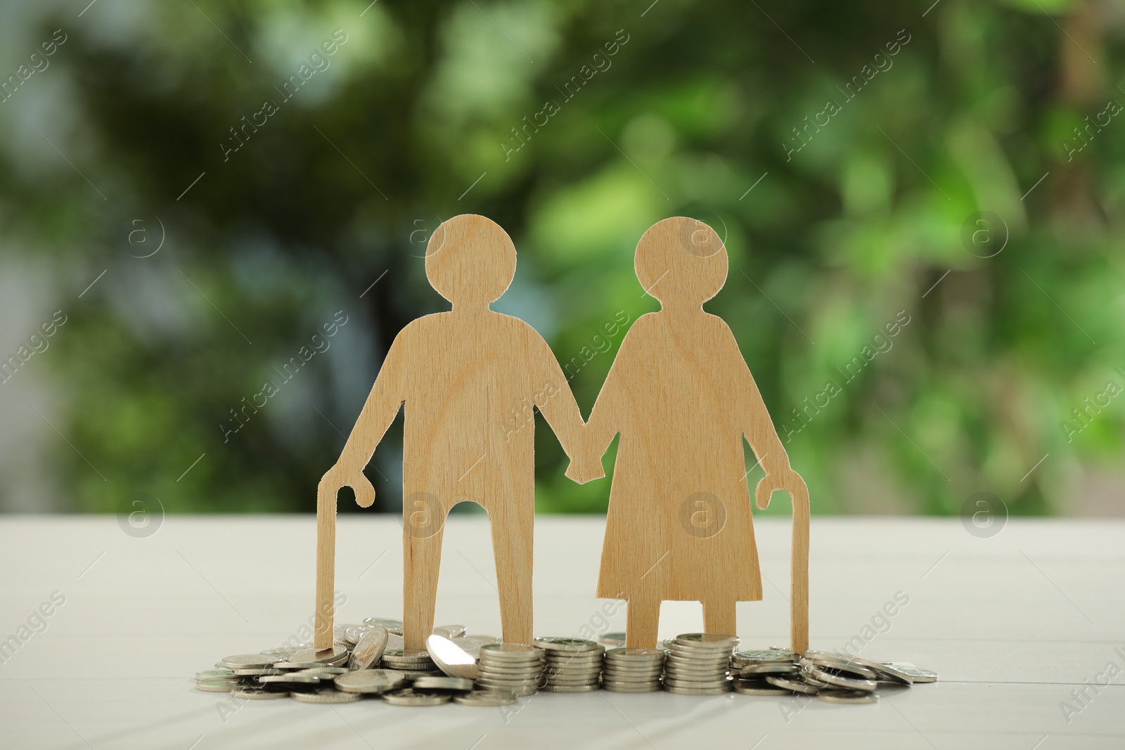 Photo of Pension savings. Figure of senior couple and coins on white table against blurred green background