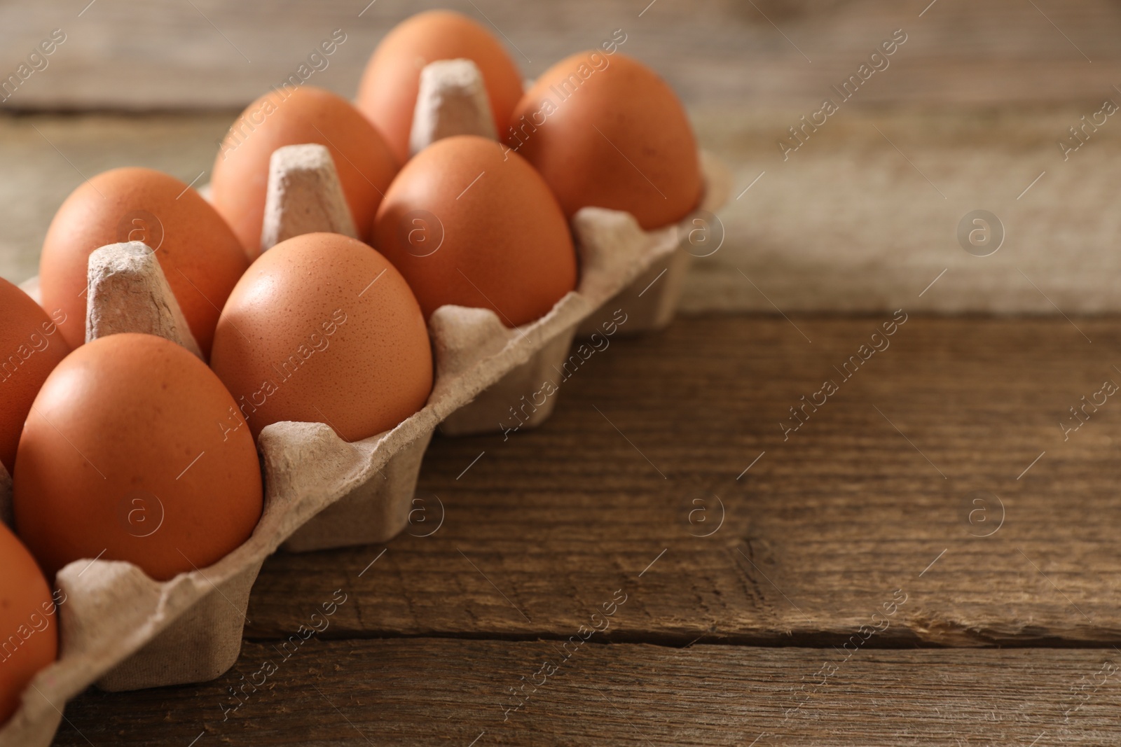 Photo of Raw chicken eggs in carton on wooden table, closeup. Space for text