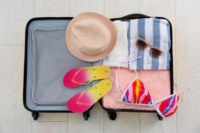 Open suitcase with female clothing and accessories on wooden background