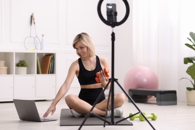 Photo of Smiling sports blogger with dumbbells streaming online fitness lesson with phone at home