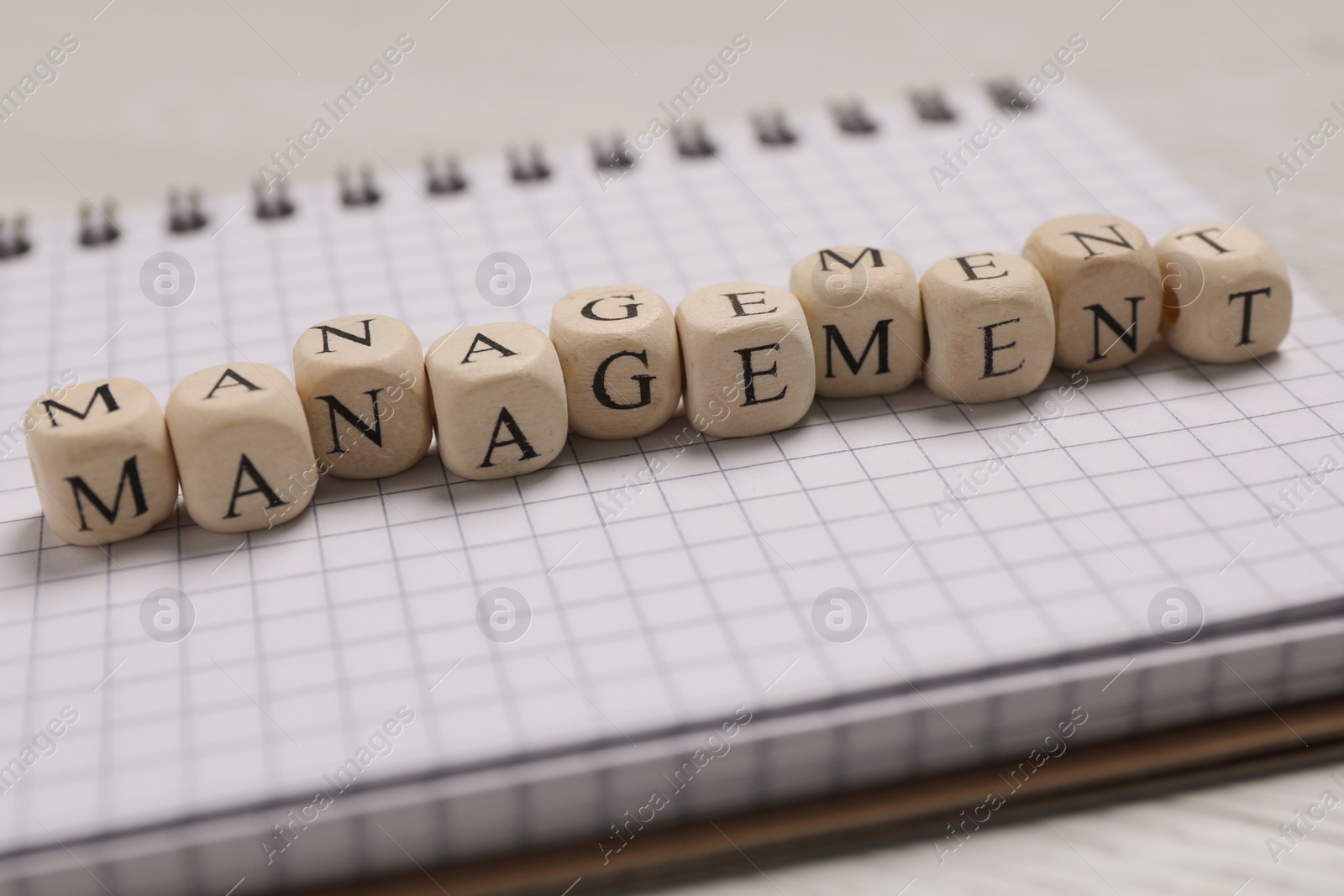 Photo of Word Management made of wooden cubes and notebook on white table, closeup