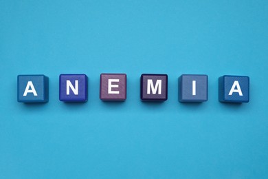 Photo of Wooden cubes with word Anemia on light blue background, flat lay