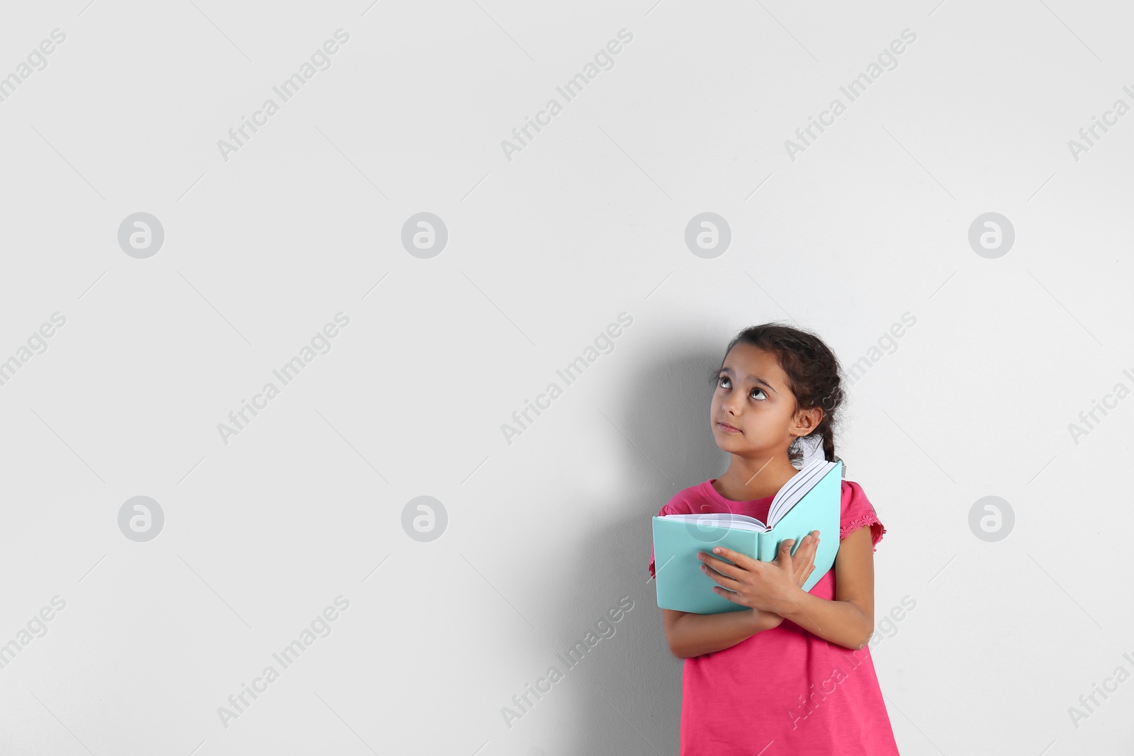 Photo of Cute little girl with book on light background,  space for text