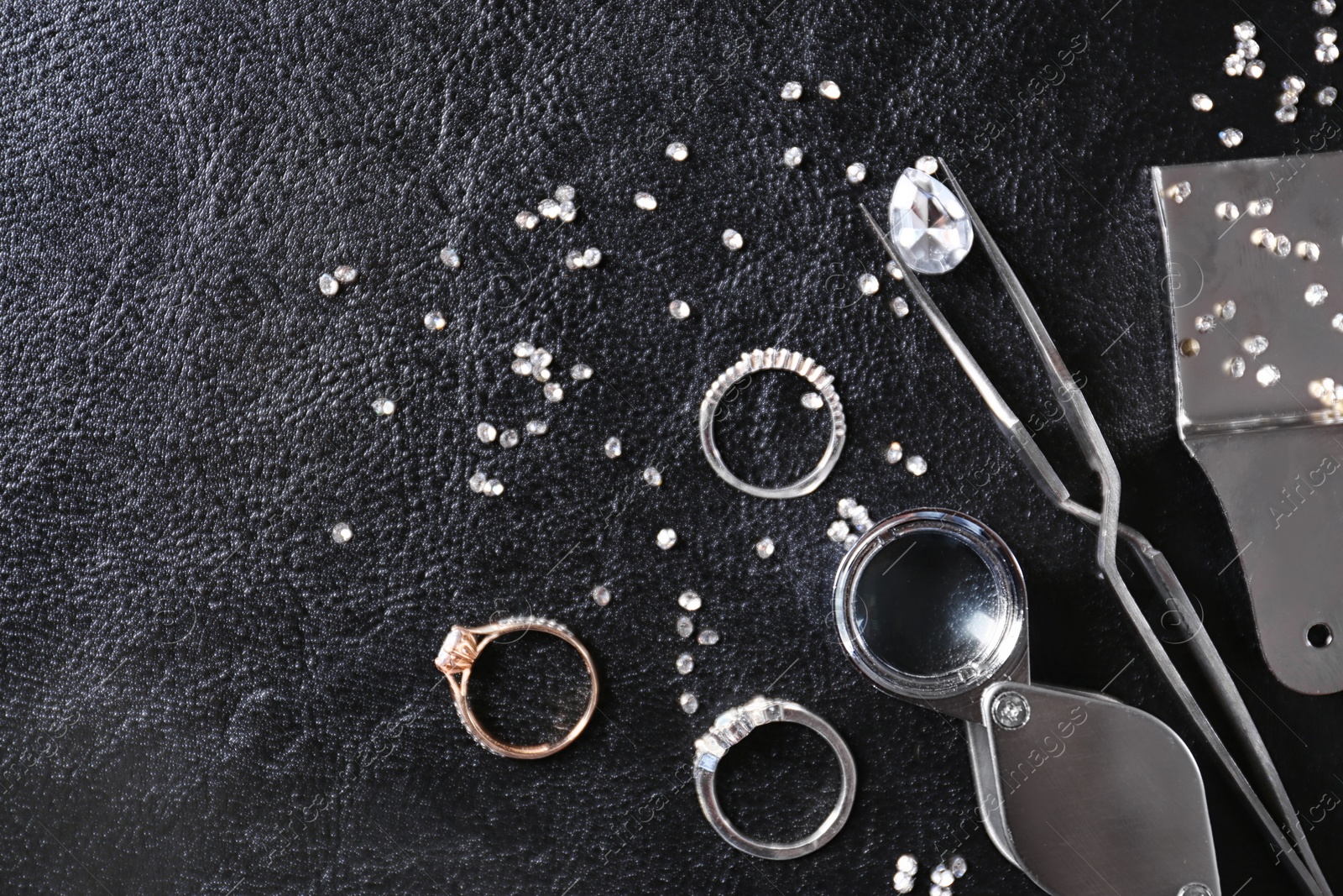 Photo of Flat lay composition with precious stones and jewelry tools on black leather background