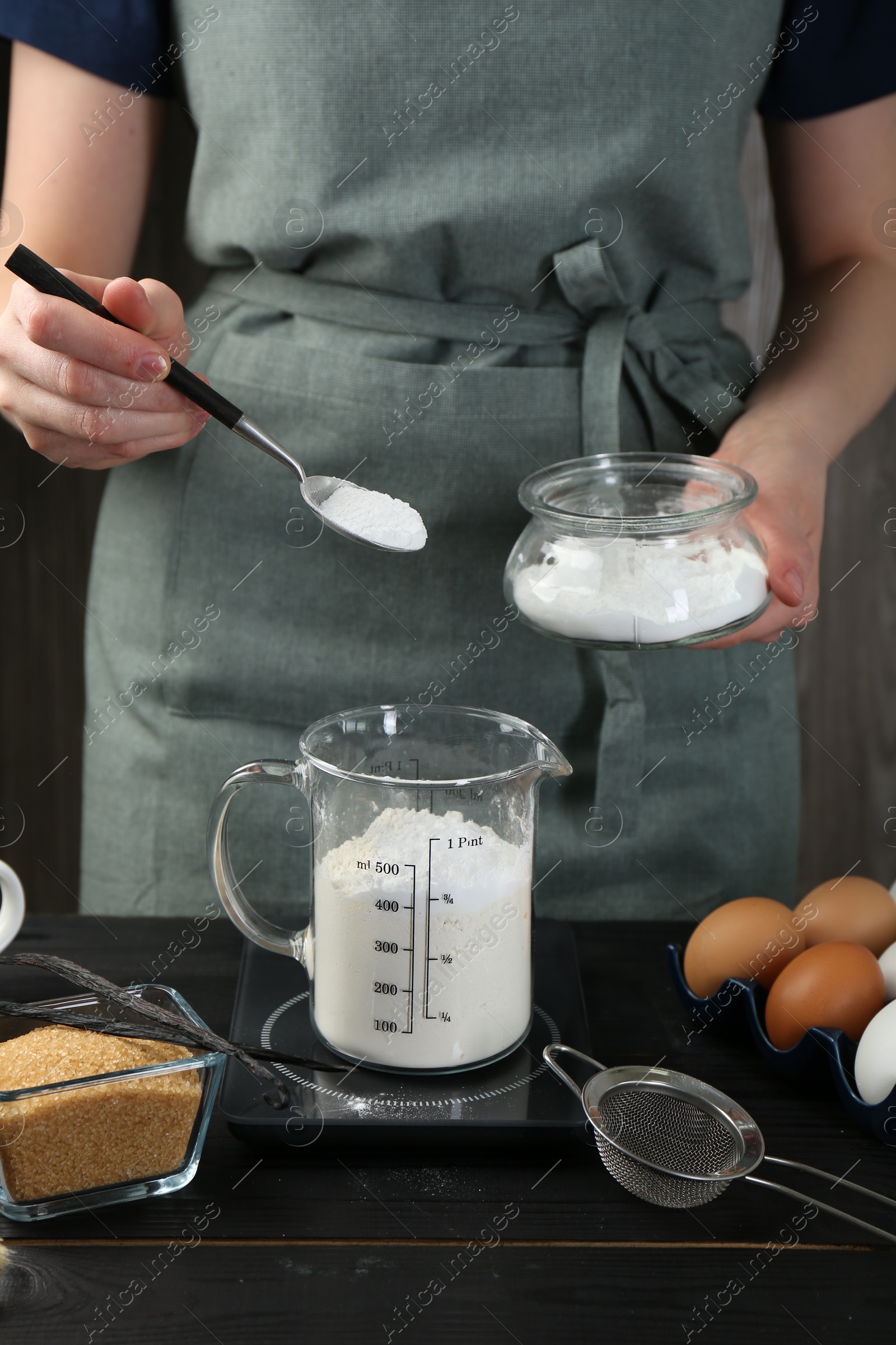 Photo of Woman adding baking powder into measuring cup at black wooden table, closeup