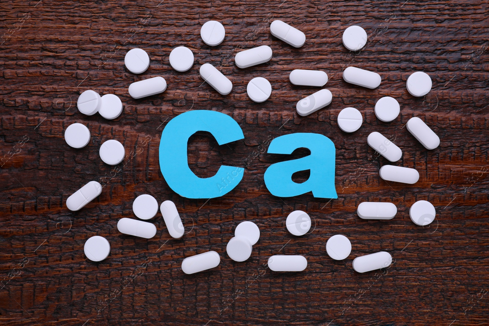 Photo of Paper symbol Ca (Calcium) and pills on wooden table, top view