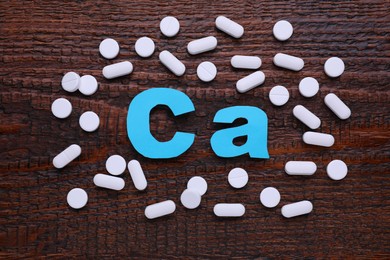 Photo of Paper symbol Ca (Calcium) and pills on wooden table, top view