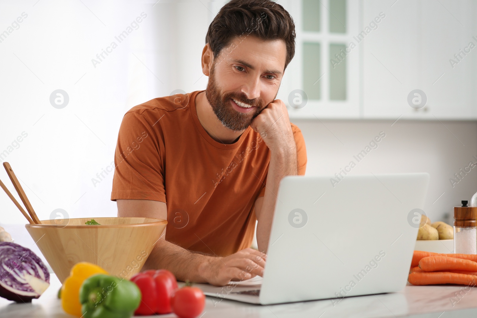 Photo of Man making dinner while watching online cooking course via laptop in kitchen