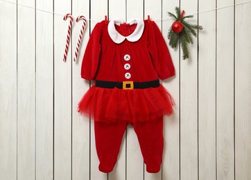 Cute Christmas baby clothes, fir branches and candy canes hanging on white wooden wall