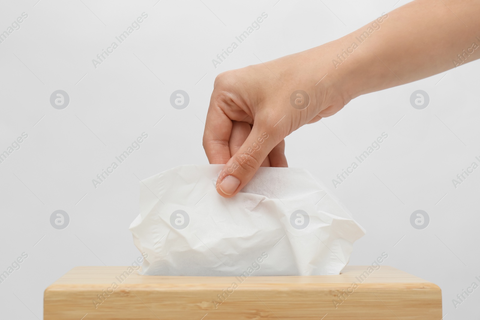 Photo of Woman taking paper tissue from holder on light background, closeup