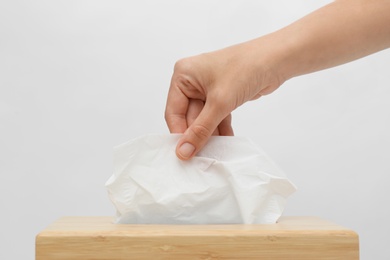 Photo of Woman taking paper tissue from holder on light background, closeup