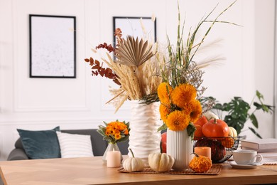 Photo of Beautiful autumn composition with bright orange flowers, pumpkins and burning candles on wooden table in room