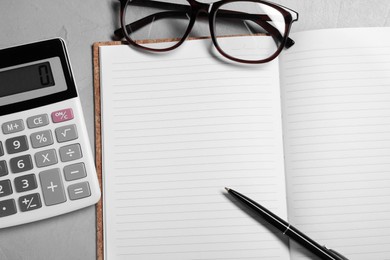 Photo of Word Bookkeeping written in notebook, calculator, glasses and pen on grey table, flat lay