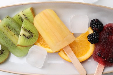 Photo of Delicious popsicles, ice cubes and fresh fruits on plate, top view