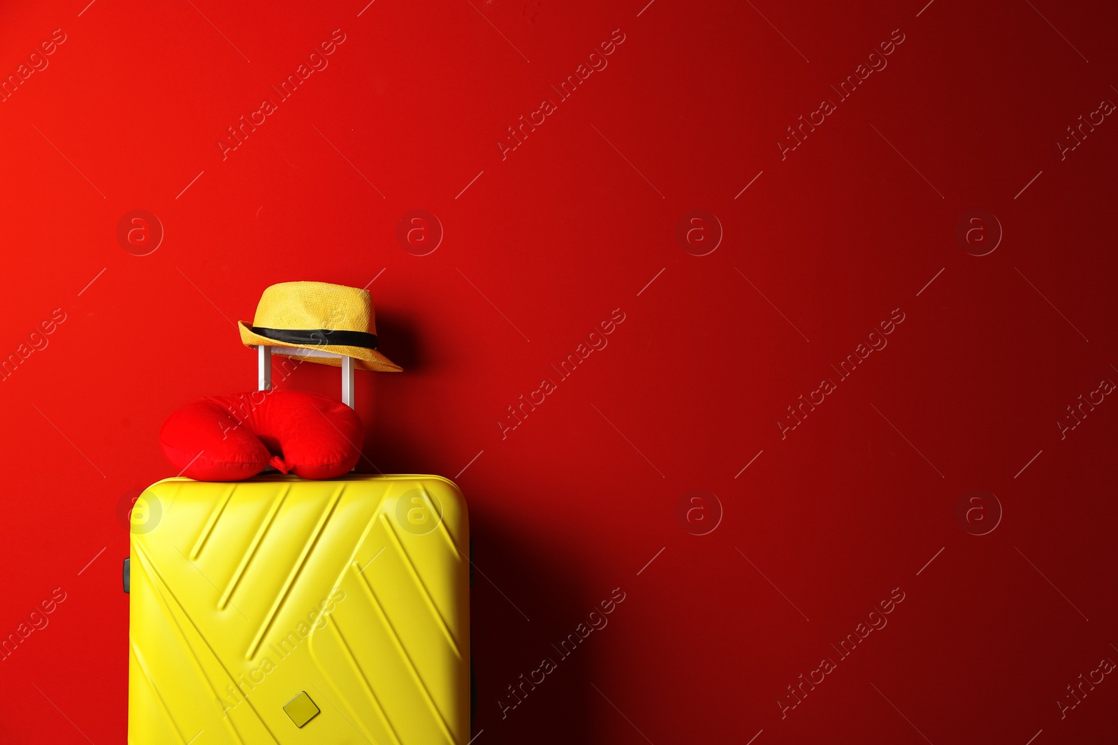 Photo of Yellow suitcase, hat and travel pillow on red background, space for text