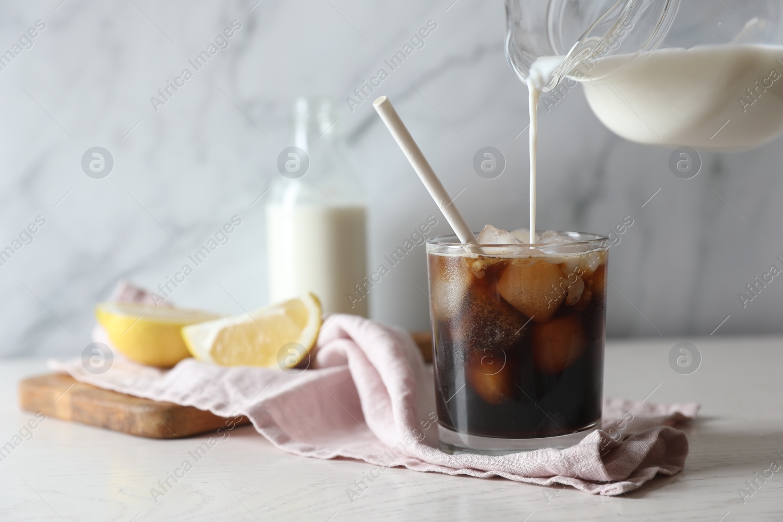 Photo of Pouring milk into glass with refreshing iced coffee at white wooden table, closeup