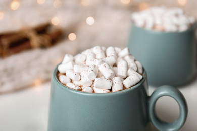 Photo of Delicious cocoa drink with marshmallows on table against blurred lights, closeup