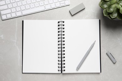 Photo of Open blank notebook, keyboard and stationery on light grey marble table, flat lay
