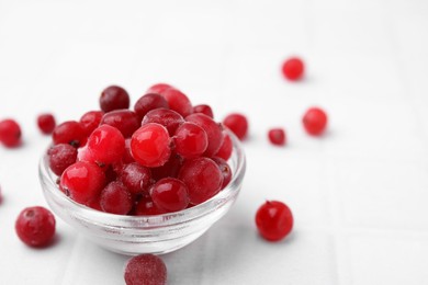 Frozen red cranberries in bowl on white table, closeup. Space for text